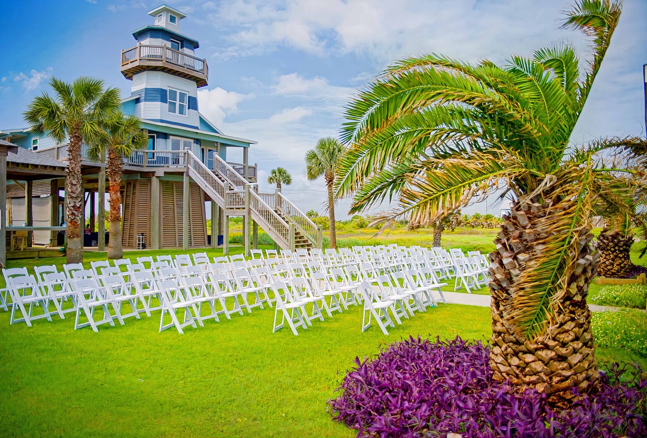 Empty white ceremony chairs beside the beachfront lighthouse at Beauty and the Beach